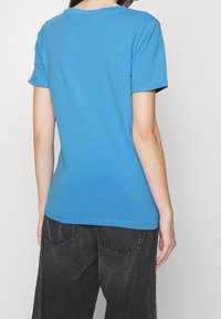 Koszulka z krótkim rękawem i okrągłym dekoltem w intensywnym, jednolitym niebieskim kolorze, wykonana z bawełny, zestawiona z ciemnoszarymi dżinsami. Koszulka ma gładką fakturę i swobodny krój.