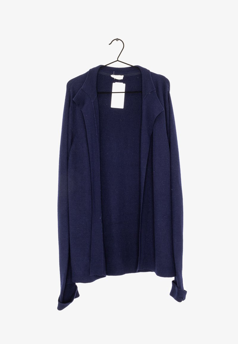 Marinblå stickad cardigan med långa ärmar, öppen front och ribbad textur. Inkluderar en tagg vid halsringningen. Hänger från en svart krok.