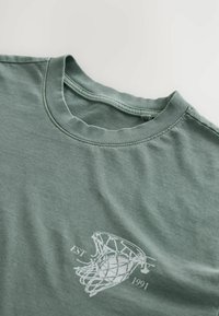 Grünes Baumwoll-T-Shirt mit rundem Ausschnitt und kurzen Ärmeln, mit einem weißen Basketballkorb-Graphic und "EST 1991". Weicher Stoff.