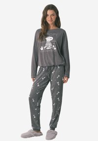 Grijs, lang mouwen pyjama top met Snoopy graphic; bijpassende grijze broek met witte Snoopy patronen en een taillekoord; gedragen met zachte pantoffels.