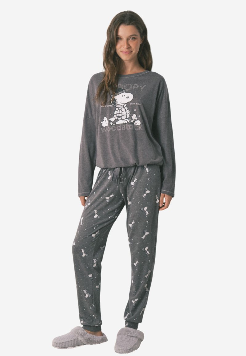Grijs, lang mouwen pyjama top met Snoopy graphic; bijpassende grijze broek met witte Snoopy patronen en een taillekoord; gedragen met zachte pantoffels.