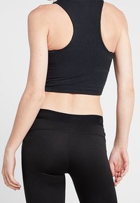 Haut court de sport côtelé noir avec un col montant, associé à des leggings noirs taille haute présentant une texture lisse et une ceinture élastique.