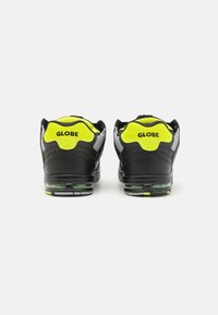 Black sneakers with gray accents, neon green heel padding, and reflective detailing; features air cushioning and textured sole.