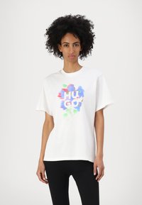 Tricou alb din bumbac, cu un design abstract colorat și textul "HUGO" în centru. Tricoul are o croială confortabilă și mâneci scurte.