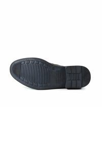 Schwarze Gummisohle mit strukturierten Grip-Mustern, ausgestattet mit horizontalen und vertikalen Rillen, verstärktem Fersenbereich und Logodetail.