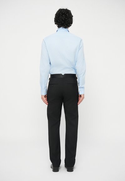 Světle modrá košile s dlouhým rukávem a špičatým límcem, doplněná o černé kalhoty rovného střihu se zadními kapsami a černým páskem.