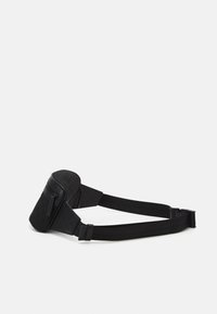 Černá kabelka přes rameno se zipovým uzávěrem, texturovanou tkaninou, nastavitelnými popruhy a kompaktním tvarem. Na jedné straně je geometrický vzor.