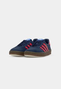 Marineblå sneakers med røde striber, struktureret gummisål, snørebåndsdesign og blå tunge med logo. Overmateriale i suede-lignende materiale.