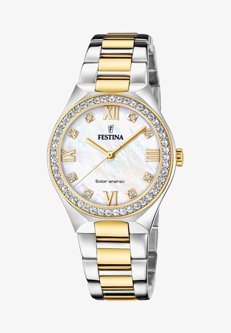Zegarek ze stali nierdzewnej w odcieniach srebra i złota z tarczą z masy perłowej, rzymskimi cyframi oraz pierścieniem wysadzanym kryształami. Mechanizm zasilany energią słoneczną.
