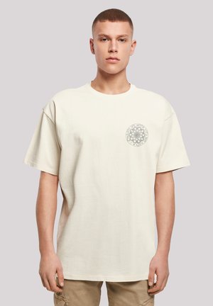 Cream-colored oversized t-shirt made of soft cotton, featuring a round neckline and a circular graphic design on the left chest.