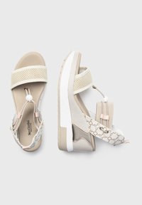 Beige sandaler med netstræk, et mønstret overdel og en chunky hvid sål. Udstyret med justerbare beslag og tekstureret overflade.