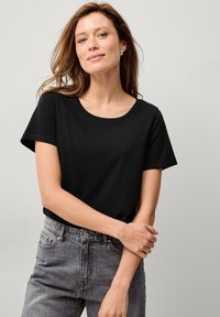 Schwarzes Kurzarm-T-Shirt mit Rundhalsausschnitt, aus weichem Stoff hergestellt. Kombiniert mit verblichenen grauen Jeans, die eine lockere Passform betonen.