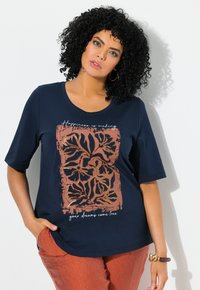 Camiseta de color azul marino con mangas cortas, presenta un diseño floral en tonos óxido y dorado, con el texto "La felicidad es hacer realidad tus sueños."