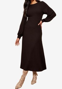 Robe noire à manches longues côtelée avec un corsage ajusté et une jupe fluide. Associée à des bottines à imprimé serpent à motifs.