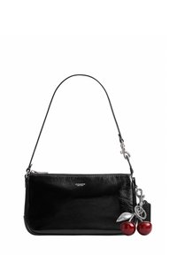 Sac à main Coach en cuir noir avec une sangle courte et un porte-clés décoratif en forme de cerise attaché sur le côté.