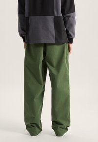 Długi rękaw w czarno-szarym, blokowym wzorze, zestawiony z luźnymi spodniami w oliwkowym odcieniu zieleni. Tkanina wydaje się miękka i przewiewna.