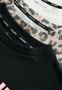 Trīs T-krekli izstādīti: melns, balts ar leopardu rakstu un pelēks. Mīksta auduma, ar apaļām apkaklēm un redzamām zīmolu etiķetēm iekšpusē.