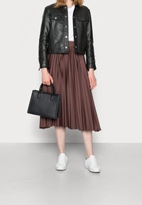 Veste en cuir noire, t-shirt blanc, jupe midi plissée marron, sac à main noir et baskets blanches. Textures lisses et couleurs contrastées.