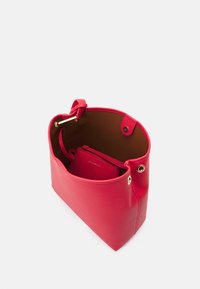 Czerwona skórzana torba typu tote o gładkiej fakturze i okrągłym otwarciu. Wnętrze wykończone brązową podszewką oraz małą dopasowaną kieszonką na zamek. Złote akcenty metalowe.