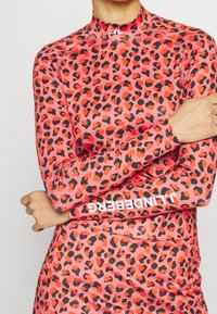 Long-sleeve rash guard in pink with black and orange leopard print. Features a mock neck and logo detail on the sleeve. Smooth, stretchy material.