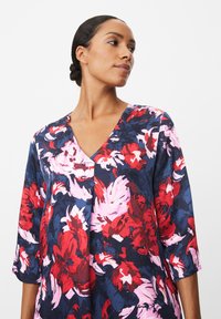 Bloemtop met een V-hals, driekwart mouwen en een donkere achtergrond met patronen in rood, roze en marineblauw. Textuurstof.