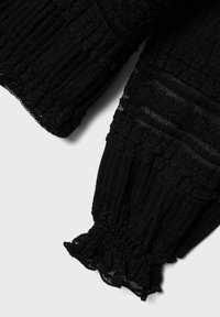Tessuto nero testurizzato con un polsino elastico arricciato. Il materiale presenta un motivo a coste, con dettagli in pizzo lungo i bordi.
