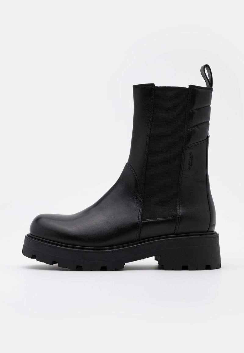 Bottes courtes noires avec un bout arrondi, en matériau brillant. Comprend des panneaux latéraux élastiques, un tirant et une semelle en caoutchouc noire texturée.
