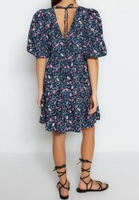 Kwiecista sukienka na granatowym tle, z bufkami, otwartym tyłem z zapięciem na troczki, warstwowym falbanym dołem, w połączeniu z czarnymi sandałami na słupku.