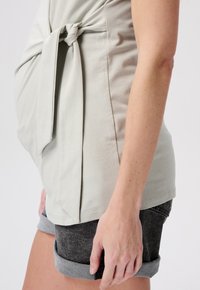 Hellgraues Oberteil mit einem Knoten-Detail vorne, kombiniert mit grauen Shorts mit umgeschlagenen Säumen. Der Stoff hat eine weiche Textur und ein lässiges Design.