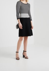 Robe rayée noir et blanc avec un haut ajusté et une jupe évasée. Tissu texturé et manches trois-quarts. Associée à des sandales à talons.