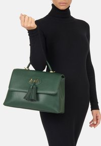 Zielona skórzana torebka z klapą, złotymi akcentami i frędzlami. Gładka faktura i uporządkowany, prostokątny kształt.