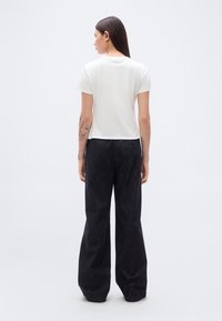 Λευκό κοντοκομμένο μπλουζάκι και μαύρο παντελόνι με φαρδείς παντελόνιες, με ψηλή μέση και διακριτική υφή. Απλός, μινιμαλιστικός σχεδιασμός χωρίς εμφανή λογότυπα.