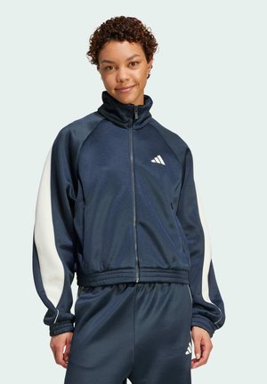 Marineblauwe zip-up jas van gladde stof, met witte accentstrepen, een hoge kraag en een geborduurd logo op de borst.