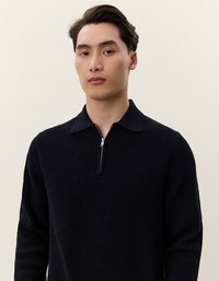 Navyblauer Strickpullover mit Reißverschlusskragen, gerippter Textur und langen Ärmeln. Der Stoff wirkt weich und gemütlich mit einer strukturierten Passform.