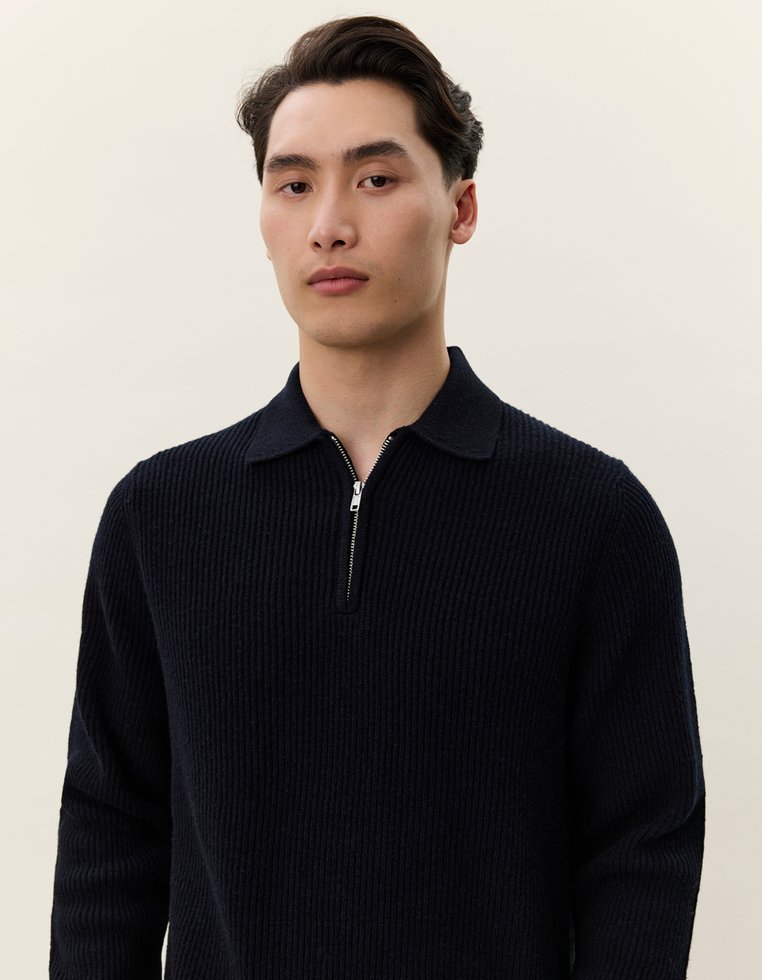 Navyblauer Strickpullover mit Reißverschlusskragen, gerippter Textur und langen Ärmeln. Der Stoff wirkt weich und gemütlich mit einer strukturierten Passform.