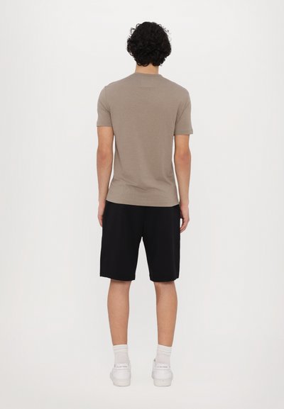 Short-sleeve, taupe T-shirt made of cotton, paired with black shorts. Model is wearing white sneakers and ankle socks. Neutral background.