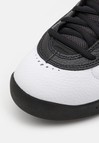 Gros plan sur la pointe d'une basket en cuir noir et blanc avec des lacets noirs et de petites perforations près du bord avant.