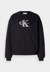 Čierna mikina vyrobená z bavlny s hrubým výstrihom a manžetami. Má predné logo s nápisom "Calvin Klein" a "CK" v striebornom vyšívaní.