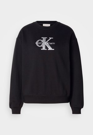Czarny sweter z bawełny z prążkowanym dekoltem i mankietami. Ma na froncie logo z napisem "Calvin Klein" oraz "CK" w srebrnym haftem.