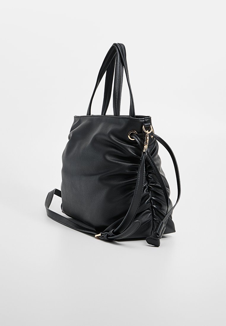 Bolso tote de cuero sintético negro con un acabado suave y texturizado. Presenta dos asas largas y un diseño lateral gather de contraste con acentos en dorado.