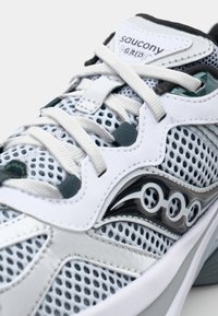 Le scarpe Saucony presentano un design leggero con una struttura in mesh grigia e bianca, accenti verde scuro in contrasto e lacci testurizzati.