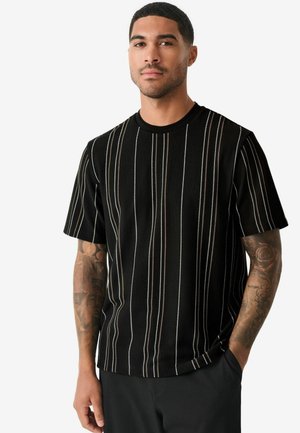 Chemise noire à manches courtes avec des rayures verticales marron, beige et blanche. Le tissu présente une texture côtelée. Encolure ronde.