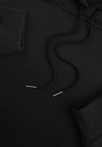 Zwarte hoodie met ribgebreide manchetten, platte trekkers met metalen aglets en een zachte textuur. Minimalistisch ontwerp zonder zichtbare logo's of patronen.