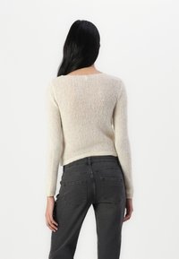 Crewneck sweater i lys cremet farve, lavet af tekstureret strikket stof; tætsiddende pasform; parret med mørkegrå jeans, bagsiden viser minimale sømdetaljer.