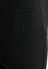 Leggings neri con una superficie liscia, vita alta e delicate cuciture lungo la vita e le tasche, che mettono in evidenza un design elegante.