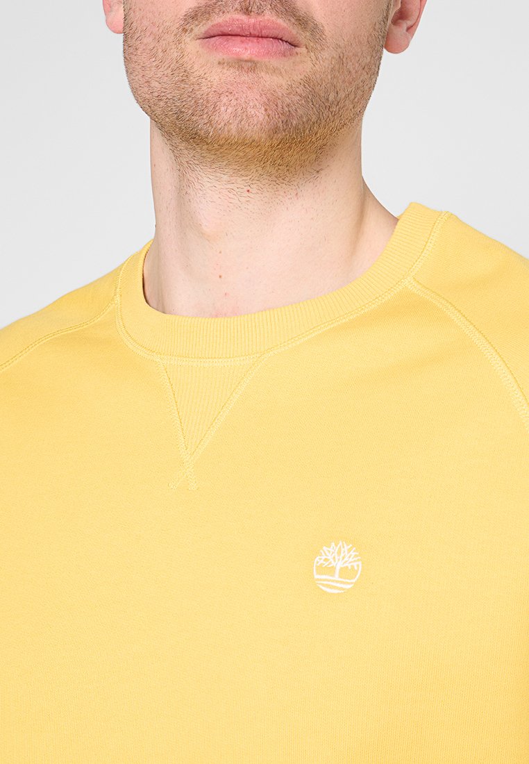 Felpa gialla con colletto a girocollo e bordi ribattuti. Presenta un piccolo logo bianco di un albero sul petto. Realizzata in tessuto morbido.