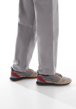 Sneaker con una tomaia in suede beige, accenti grigi, tacco rosso e suola scura. Abbinati a pantaloni a sigaretta grigi chiari.