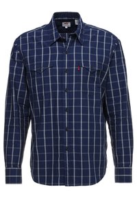 Chemise en flanelle à manches longues de couleur marine avec un motif à carreaux blancs, dotée de deux poches poitrine et d'une fermeture à boutons, fabriquée à partir d'un tissu doux et texturé.