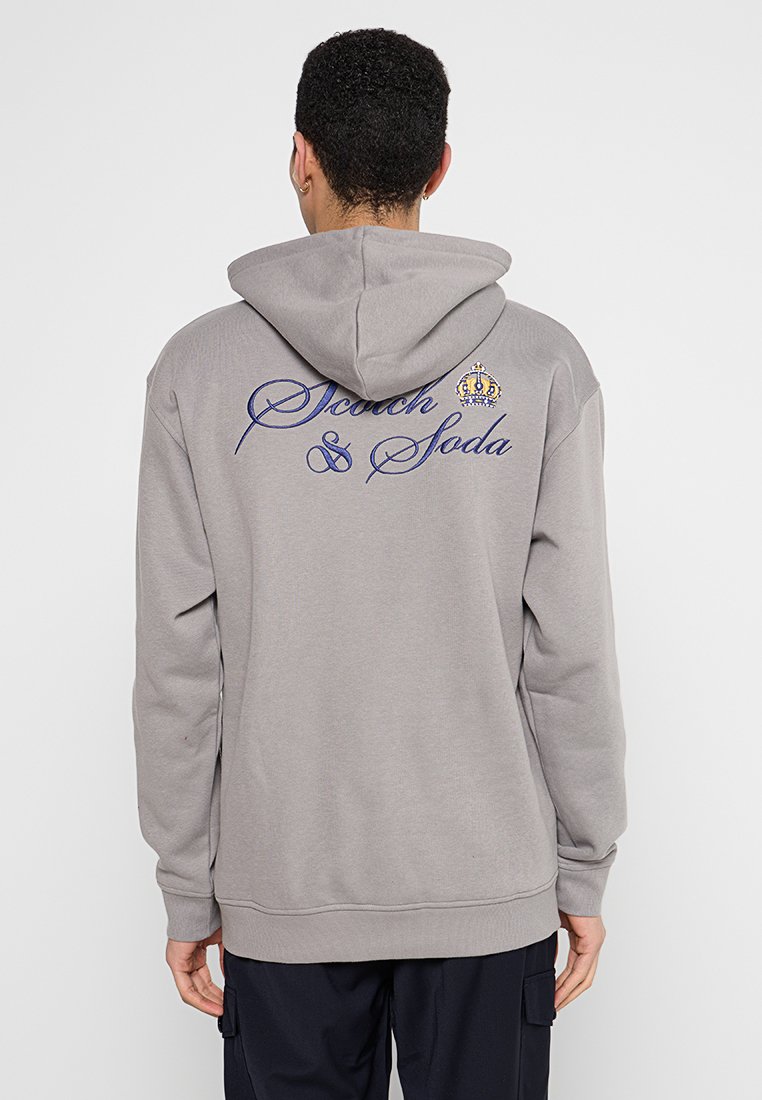 Grijze hoodie met een trekkoord en een groot blauw geborduurd logo "Scotch & Soda" met een kroon detail op de achterkant. Zachte katoenmix.