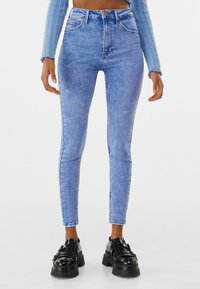 Hoge taille blauwe denim skinny jeans met een vervaagde afwerking, voorzien van subtiele slijtage en een traditioneel pocketontwerp. Draagt met chunky zwarte schoenen.
